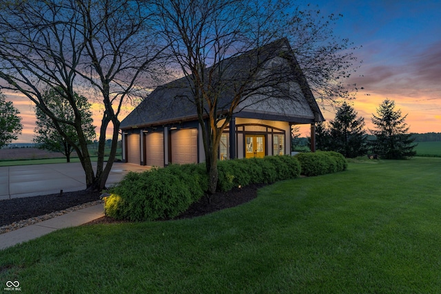 property exterior at dusk with an attached garage, a yard, and driveway