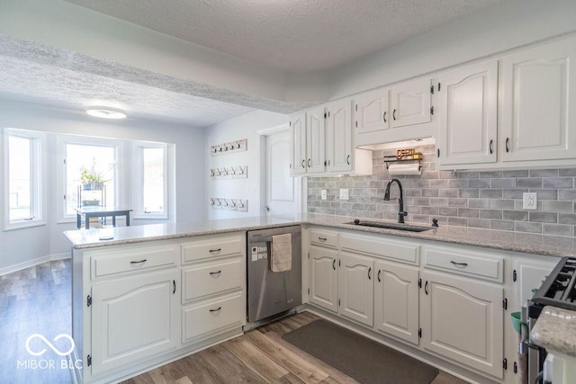 kitchen with a peninsula, a textured ceiling, a sink, light wood-style flooring, and appliances with stainless steel finishes