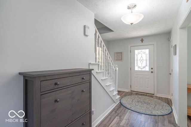 entryway with stairway, baseboards, a textured ceiling, and wood finished floors