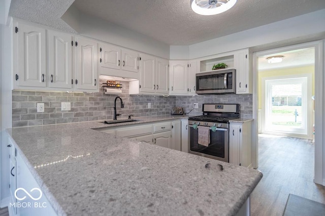kitchen featuring open shelves, a textured ceiling, white cabinets, a sink, and appliances with stainless steel finishes