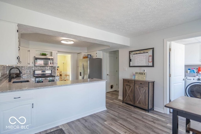 kitchen with washer / clothes dryer, a textured ceiling, a sink, light wood finished floors, and appliances with stainless steel finishes