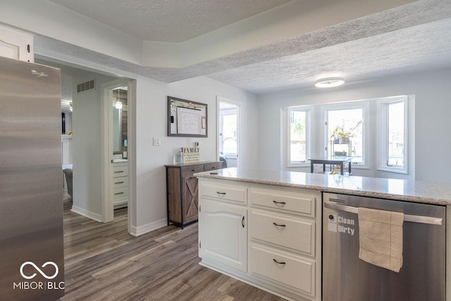 kitchen with a textured ceiling, stainless steel appliances, white cabinetry, wood finished floors, and visible vents