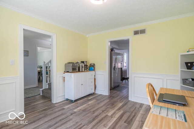 home office featuring visible vents, ornamental molding, light wood-style flooring, and a wainscoted wall