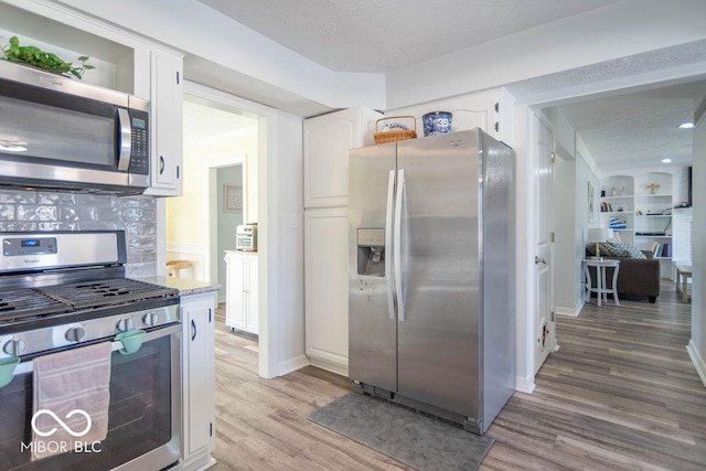 kitchen with light wood-style floors, decorative backsplash, white cabinetry, and appliances with stainless steel finishes