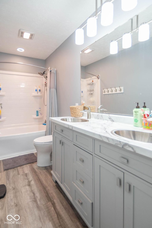 full bath with double vanity, visible vents, wood finished floors, a sink, and toilet
