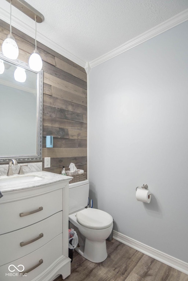 half bathroom with crown molding, vanity, wood finished floors, toilet, and a textured ceiling
