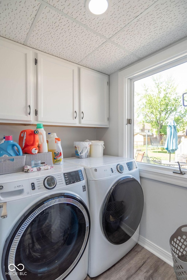 clothes washing area featuring cabinet space, baseboards, wood finished floors, and washing machine and clothes dryer