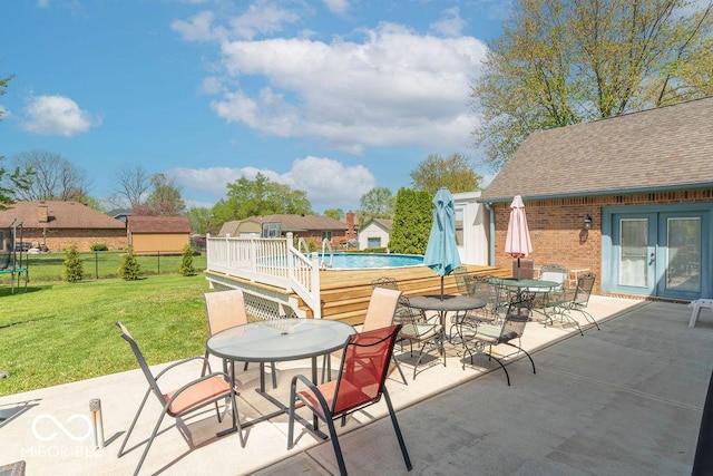 view of patio featuring outdoor dining area, a trampoline, a wooden deck, fence, and a fenced in pool