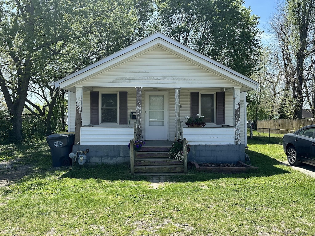 bungalow featuring covered porch, fence, and a front lawn