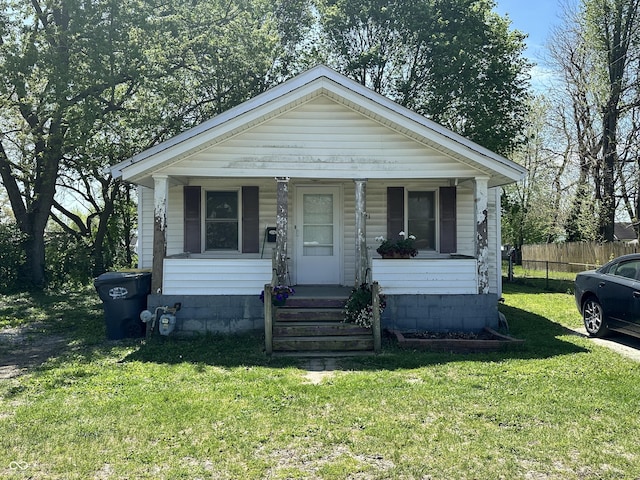 bungalow featuring covered porch, fence, and a front lawn