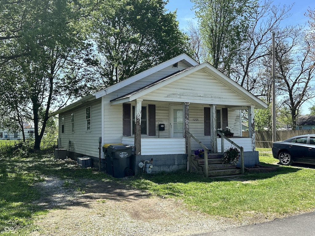 bungalow-style house with a porch, central AC, fence, and a front lawn