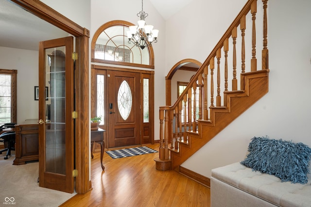foyer featuring an inviting chandelier, baseboards, stairway, arched walkways, and light wood-style flooring