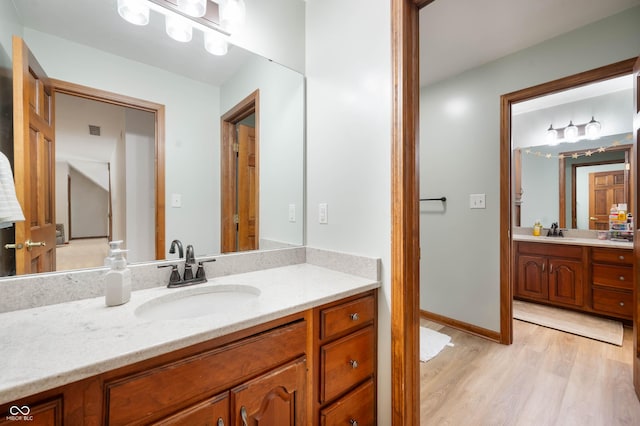 bathroom featuring visible vents, a sink, two vanities, and wood finished floors