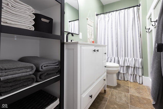 bathroom featuring stone tile floors, toilet, curtained shower, and vanity