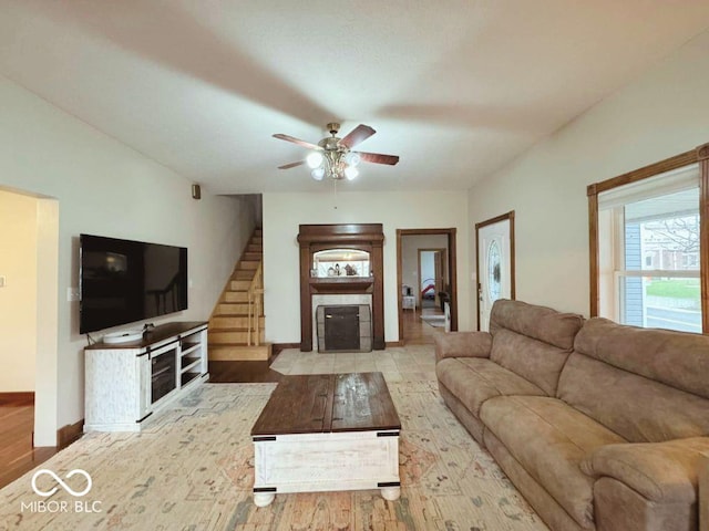 living area with ceiling fan, baseboards, a fireplace with flush hearth, wood finished floors, and stairway