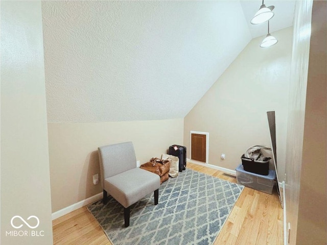 living area with visible vents, baseboards, wood finished floors, and vaulted ceiling