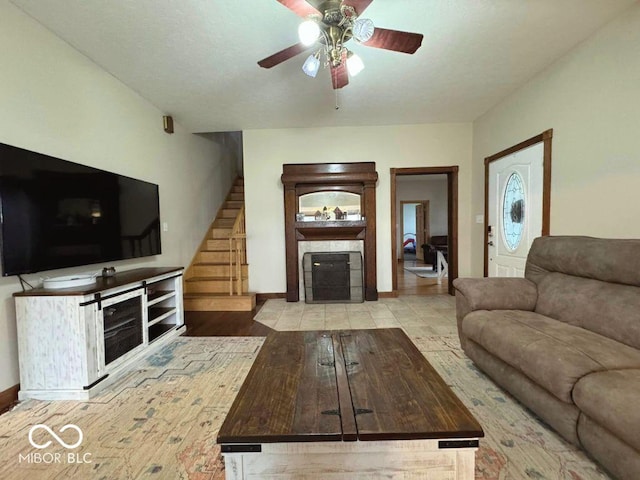 living area featuring a ceiling fan, baseboards, a fireplace with flush hearth, wood finished floors, and stairway