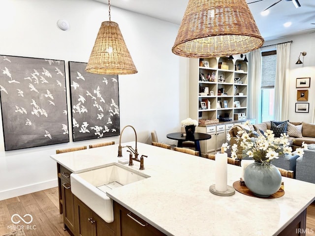 kitchen featuring dark brown cabinetry, decorative light fixtures, a sink, open floor plan, and light wood-style floors