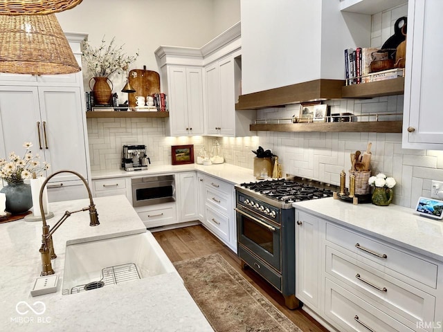kitchen featuring gas range, open shelves, a sink, custom range hood, and dark wood-type flooring