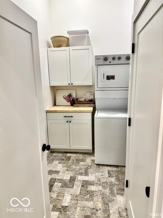 clothes washing area with cabinet space, brick patterned floor, and stacked washer and clothes dryer