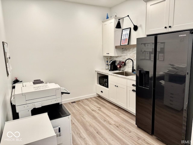 kitchen with white cabinets, a sink, light wood-style flooring, decorative backsplash, and black appliances