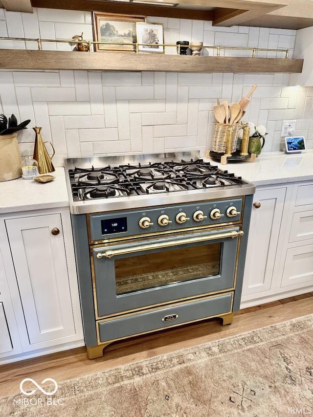 interior space with range with gas stovetop, light wood-style flooring, white cabinetry, and backsplash