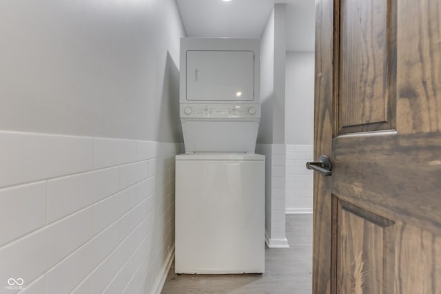 laundry room featuring tile walls, stacked washer / drying machine, wainscoting, and wood finished floors