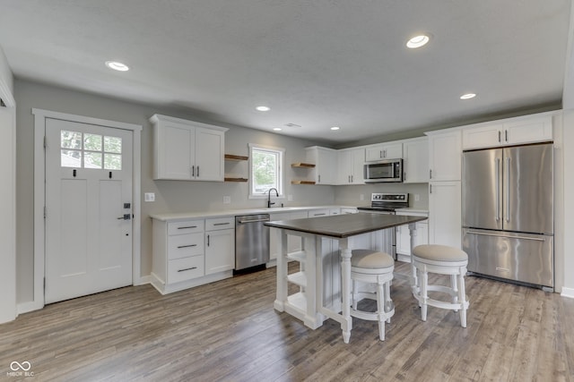 kitchen with stainless steel appliances, open shelves, a sink, white cabinets, and a breakfast bar