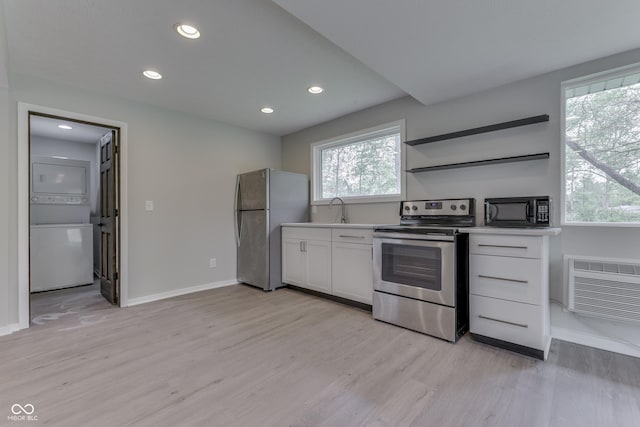 kitchen featuring appliances with stainless steel finishes, stacked washer / drying machine, light wood finished floors, white cabinetry, and baseboards