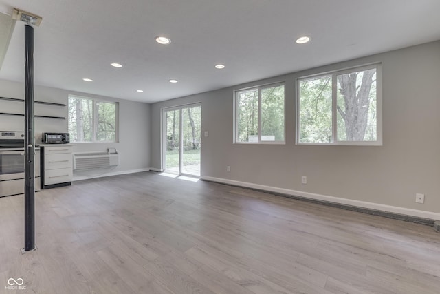 unfurnished living room with recessed lighting, baseboards, light wood finished floors, and an AC wall unit