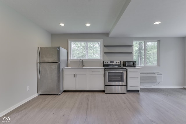 kitchen featuring appliances with stainless steel finishes, a wall unit AC, baseboards, light wood-type flooring, and healthy amount of natural light