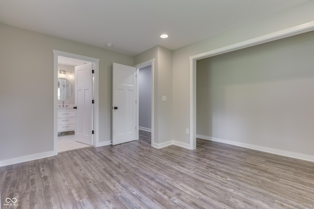 unfurnished bedroom featuring wood finished floors, baseboards, recessed lighting, and ensuite bath