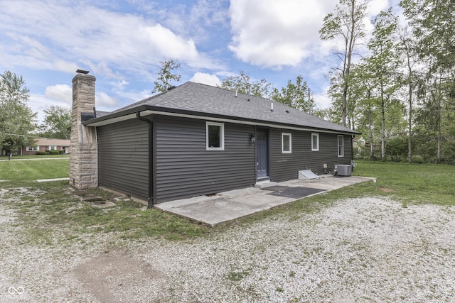 rear view of house featuring a chimney, cooling unit, roof with shingles, a patio, and a lawn