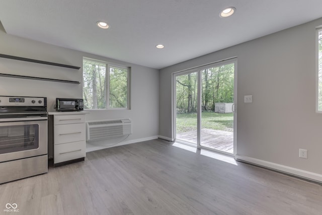 kitchen featuring electric stove, an AC wall unit, plenty of natural light, white cabinetry, and recessed lighting