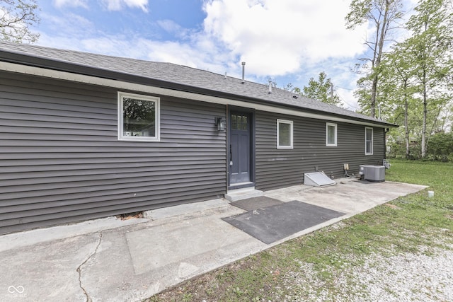 rear view of house with a patio, cooling unit, a lawn, and roof with shingles