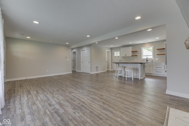 unfurnished living room featuring recessed lighting, light wood-style flooring, baseboards, and a sink