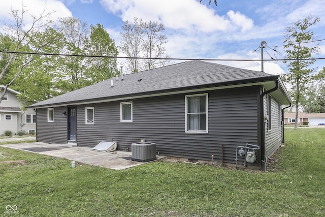 rear view of house with a patio area, central air condition unit, a lawn, and roof with shingles