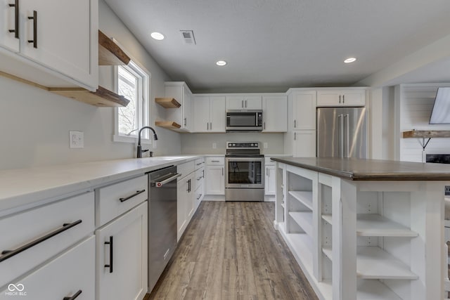 kitchen featuring open shelves, stainless steel appliances, a sink, white cabinets, and wood finished floors