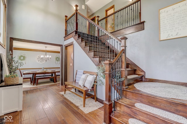 stairway featuring wood-type flooring, crown molding, a notable chandelier, and a towering ceiling