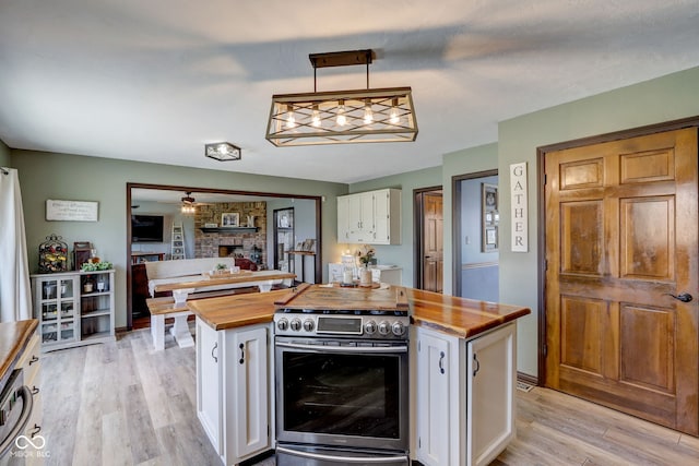 kitchen with a kitchen island, wooden counters, white cabinetry, light wood-style flooring, and stainless steel range