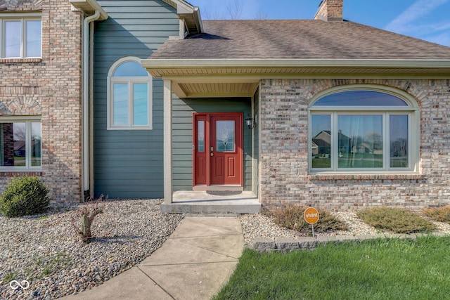 doorway to property featuring brick siding, a shingled roof, and a chimney