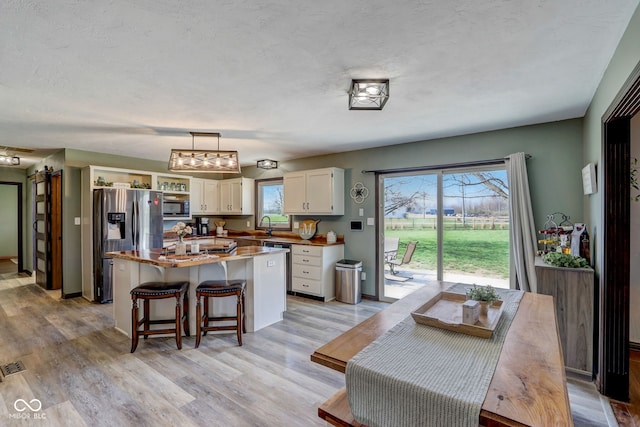 kitchen with a center island, white cabinetry, a sink, light wood-style flooring, and appliances with stainless steel finishes