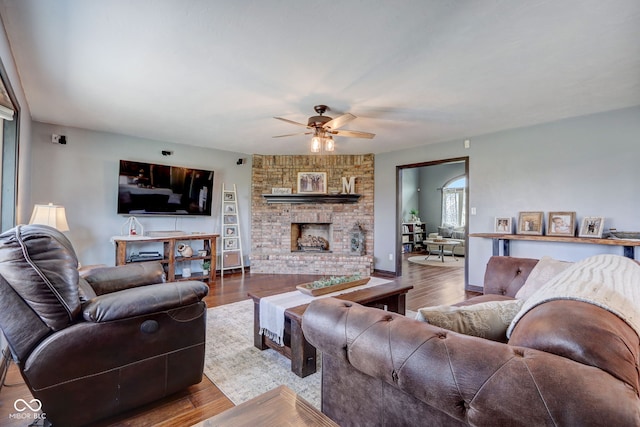 living area with a ceiling fan, a brick fireplace, and wood finished floors
