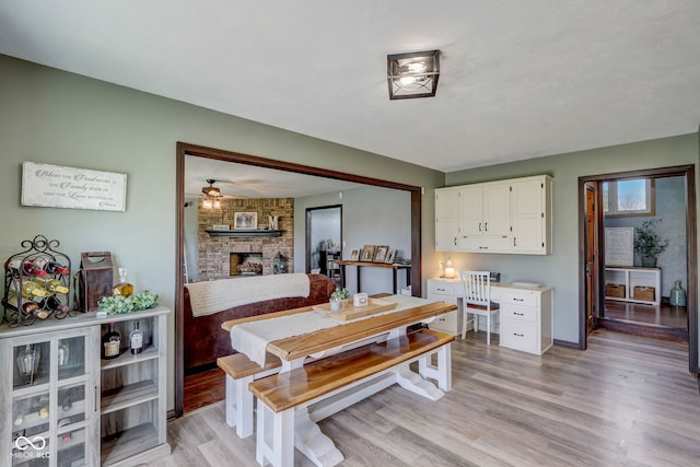 dining room featuring baseboards, light wood finished floors, ceiling fan, and a fireplace