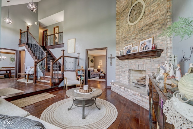 living area with wood-type flooring, an inviting chandelier, stairs, a brick fireplace, and a high ceiling