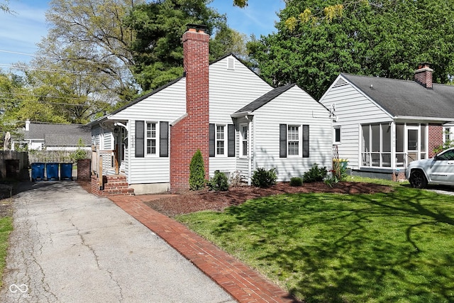 view of front of property with fence, a chimney, a sunroom, and a front lawn