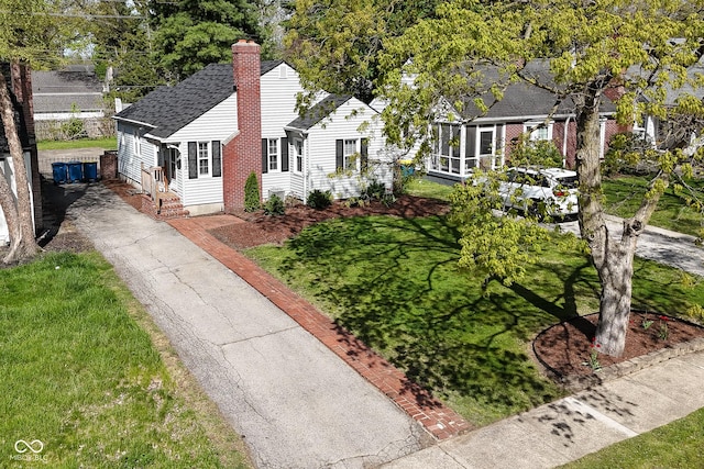 bungalow-style home with a front yard, roof with shingles, driveway, and a chimney