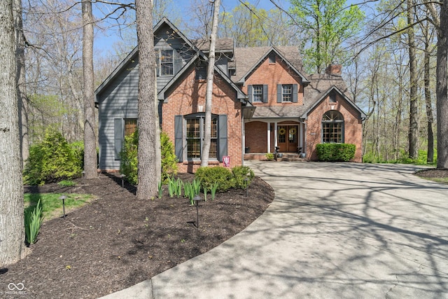 craftsman house with covered porch, brick siding, driveway, and a chimney