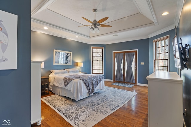 bedroom with baseboards, wood finished floors, a tray ceiling, and multiple windows
