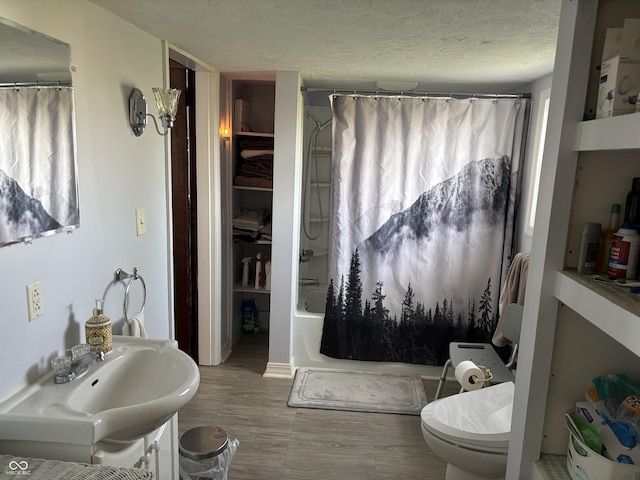 bathroom featuring a sink, a textured ceiling, shower / bathtub combination with curtain, and toilet